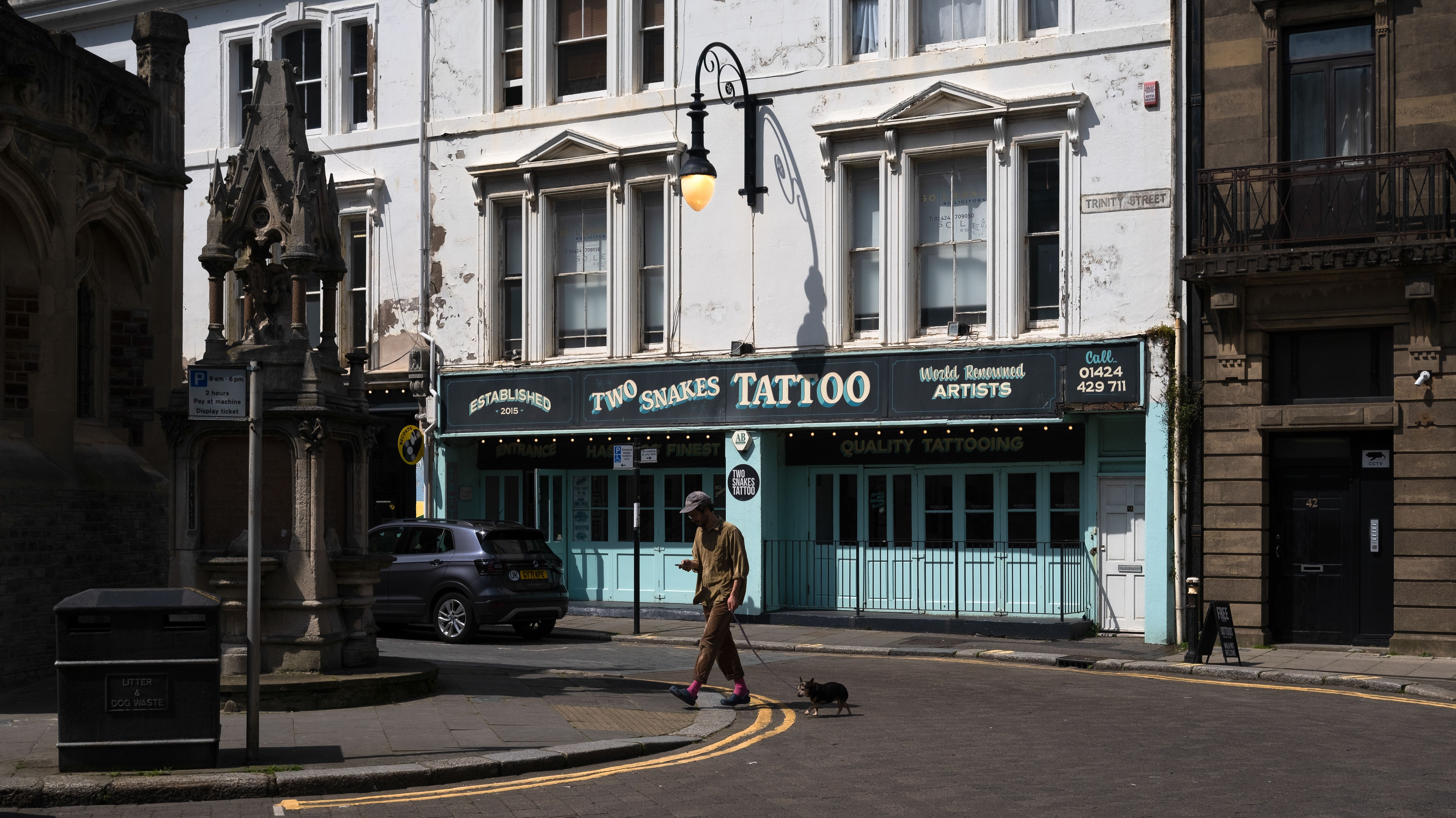 Straathoek in Hastings met een tattooshop en een voorbijganger in het ochtendlicht