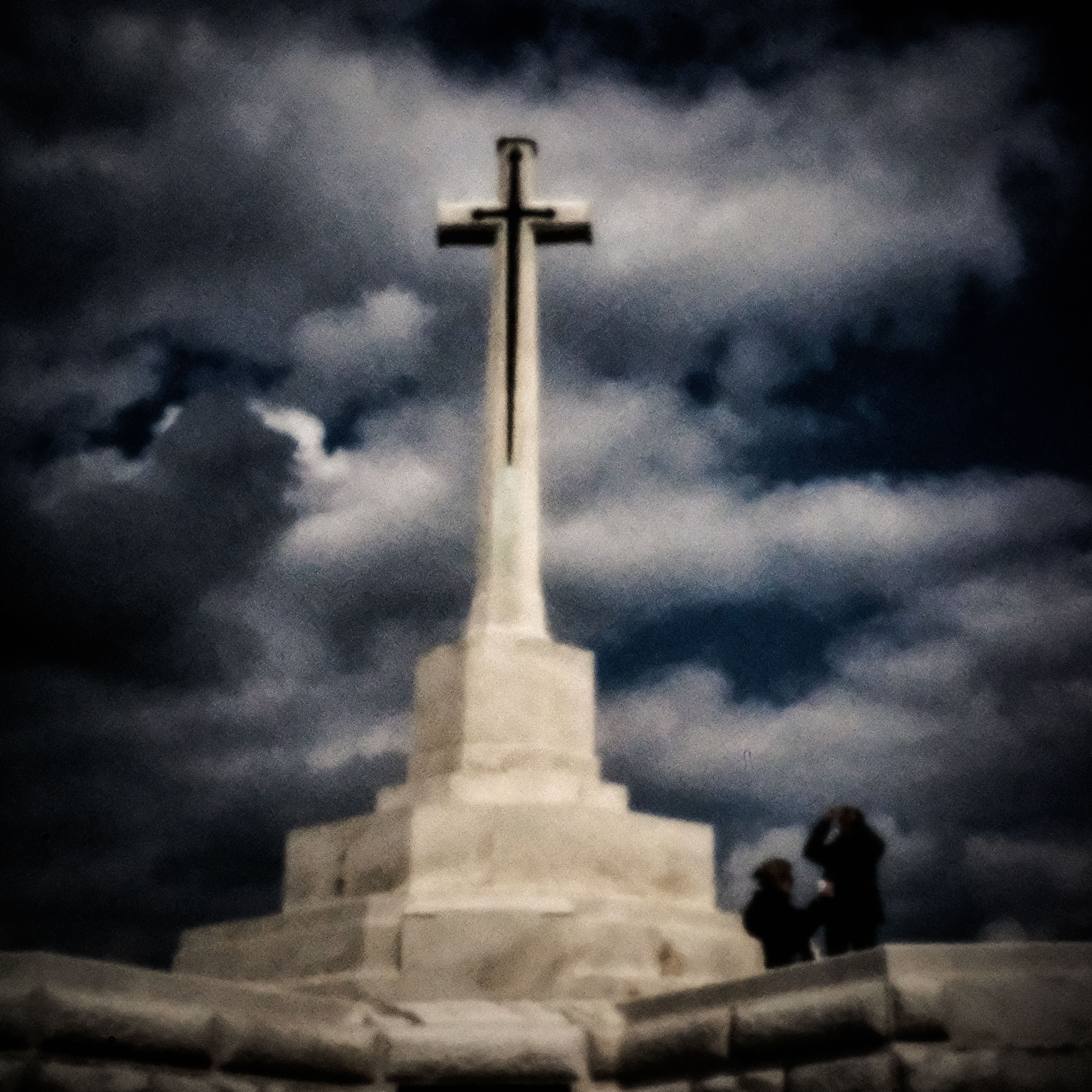 Wit oorlogsmonument met kruis onder een dreigende wolkenlucht bij Ieper