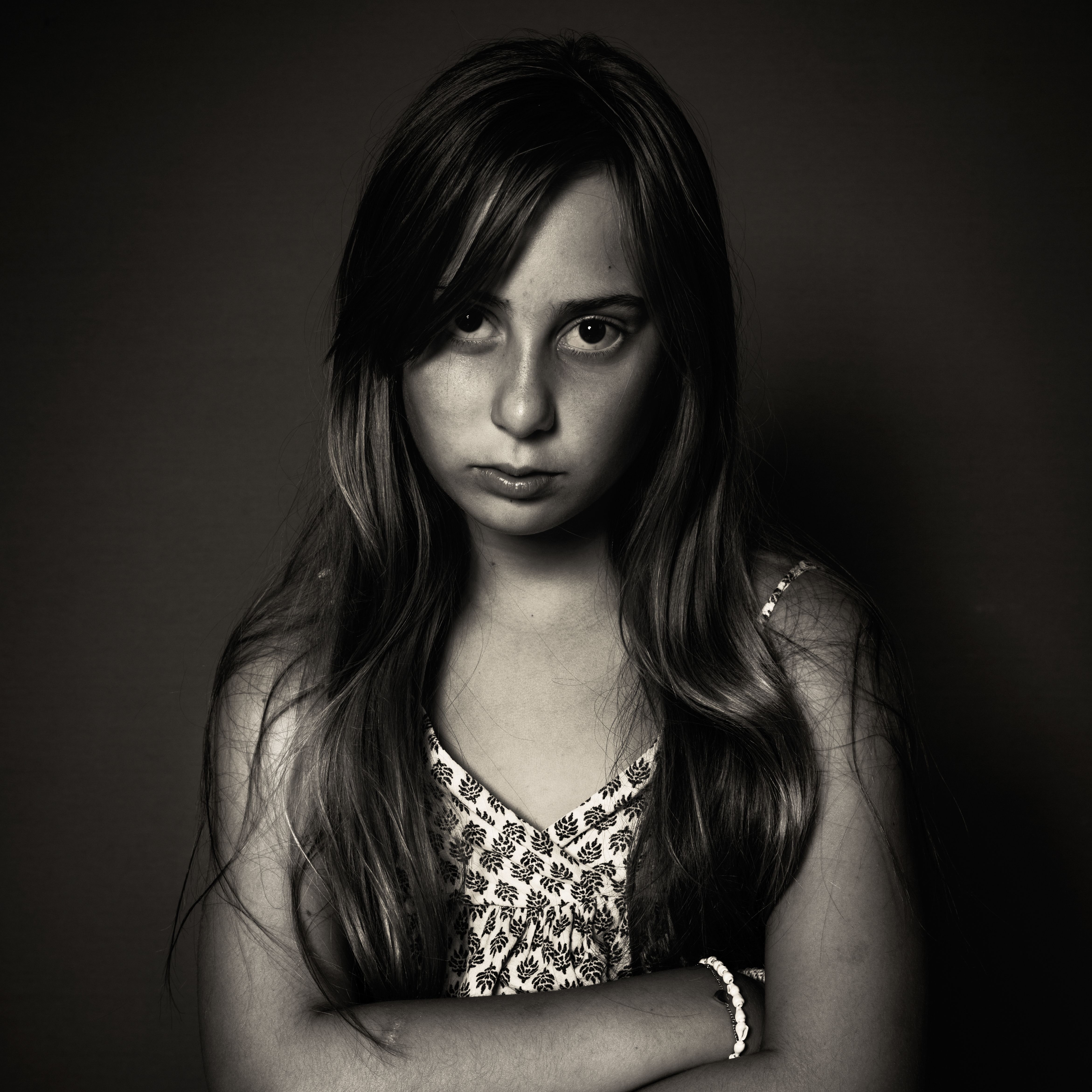 Portret van een meisje met lang haar en gekruiste armen, tegen een donkere achtergrond